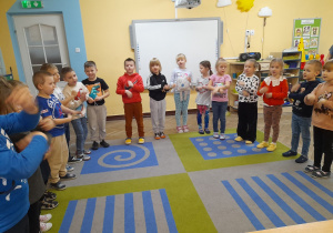 Dzieci stoją w półkolu i śpiewają piosenkę dla zaproszonego gościa.