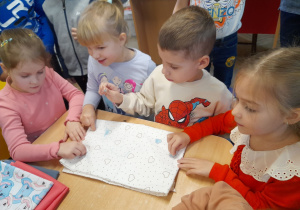 Czworo dzieci przykucnęło przy stole i rysuje kredą krawiecką na tkaninie w serduszka.