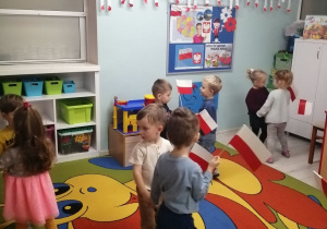 Dzieci tańczą w małych kółeczkach z flagami.