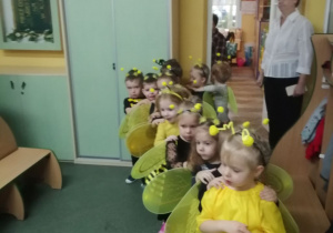 Dzieci w przebraniach pszczółek ustawione w "pociąg" stoją w holu przedszkola.