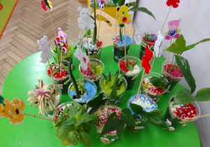 Na stoliku stoją "szalone kwiatki" - małe, zielone dekoracje wykonane przez dzieci na warsztatach.