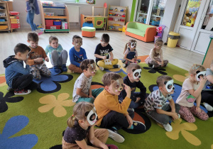 Dzieci z grupy siedzą na dywanie w maskach przedstawiających wizerunki misiów.