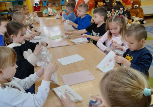 Dzieci siedzą przy wspólnym stole i pakują mydełka do papierowych torebek.
