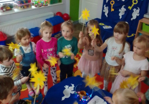 Dzieci z różdżkami w rękach czarują przy stole do wróżb. W tle dekoracja.