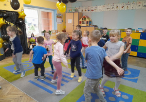 Dzieci wesoło tańczą na dywanie przy muzyce.