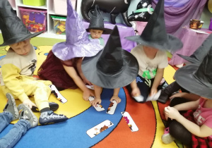 Dzieci siedzą na dywanie i układają obrazki czarownicy z części.