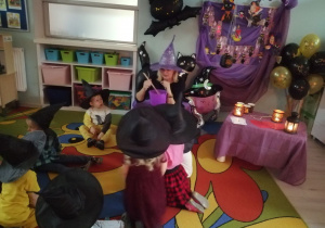 „Pszczółki” siedzą na dywanie , przed nimi nauczyciel w fioletowym kapeluszu czarownicy miesza w kociołku wróżby. W tle dekoracja z okazji Andrzejek.