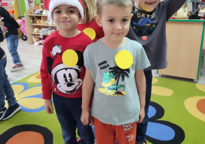 Tymek, Eryk, Franio i Anastazja w trakcie zabawy ruchowej stoją w obręczy. Każde z dzieci ma ze sobą naklejkę w kształcie żółtego koła.