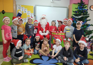 Dzieci z grupy Biedronek stoją ustawione wokół Świętego Mikołaja. W tle widać świąteczną choinkę.