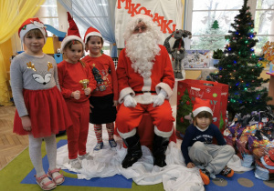 Ala, Oliwia, Ala i Maksio pozują do zdjęcia ze Świętym Mikołajem na tle mikołajkowej dekoracji.