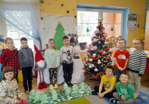 Przedszkolaki stoją obok świątecznej dekoracji, a przed nimi na podłodze leżą wykonane "świąteczne dywany i choinki".