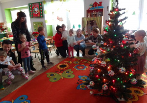 Uczestnicy warsztatów zgromadzeni wokół choinki wspólnie śpiewają piosenkę „Święta”.