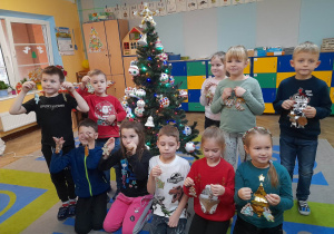 Dzieci stoją przy ubranej choince i prezentują ozdobione przez siebie pierniki.
