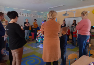 Dzieci razem z rodzicami stoją na dywanie wokół ubranej choinki i wspólnie śpiewają piosenkę „Kolędujemy” naśladując jej treść za pomocą ruchu.
