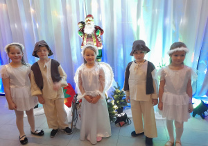 Alicja, Krzyś, Alicja, Bruno i Vanessa pozują do zdjęcia w Centrum Teatru Muzyki i Tańca. Dziewczynki ubrane są w stroje aniołków, a chłopcy w stroje pastuszków. W tle dekoracja świąteczna.