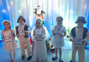 Pięcioro dzieci stoi na tle dekoracji świątecznej w Centrum Teatru Muzyki i Tańca. Przedszkolaki trzymają przed sobą dyplomy.