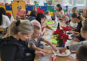 Dzieci z grupy Biedronek wraz z rodzicami siedzą przy stołach i ozdabiają świąteczne pierniczki