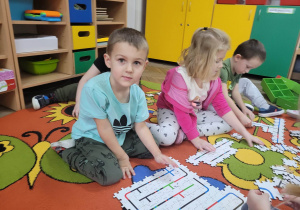 Eryk, Anastazja i Bartuś siedzą na dywanie i układają puzzle z fragmentami ścieżek dla ozobotów