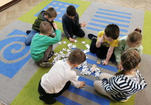 "Słoneczka" siedzą na dywanie i układają puzzle z fragmentami ścieżek dla ozobotów.