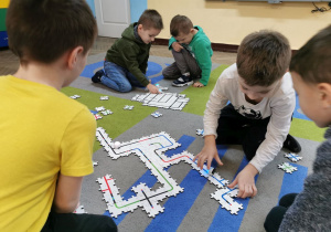Krzyś, Mieszko, Oskar i Igor w swoich parach na dywanie obserwują jak poruszają się ich ozoboty po wcześniej ułożonej ścieżce z puzzli.