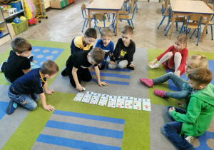 "Słoneczka" siedzą na dywanie, Mieszko dokłada cyfrę 9 do obrazka z wizerunkiem 9 bałwanków.