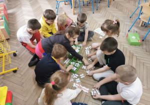 Dzieci rozkładaja na podłodze drewniane puzzle, które wyciagaja z pudełek.