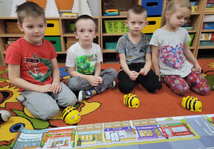 Filip, Kacper, Bartuś i Lena z grupy Biedronek siedzą przed matą do kodowania. Obok dzieci leżą pszczółki Bee Bot