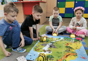 Hubert, Mieszko, Bruno i Gabrysia siedzą na dywanie wokół maty skarbów. Przyglądają się jak porusza się na macie pszczółka Bee Bot.
