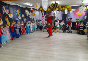 Dzieci poruszają się po kole przy muzyce. Na środku stoi wodzirej w stroju klauna z mikrofonem w ręku. W tle dekoracja.