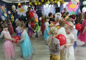 Dzieci stoją w parach naprzeciwko siebie i trzymają brzuchami balony w kolorze czerwonym. Z lewej strony stoi wodzirej "Alex" z mikrofonem w ręku, a z prawej Pani Małgosia. W tle dekoracja balowa.