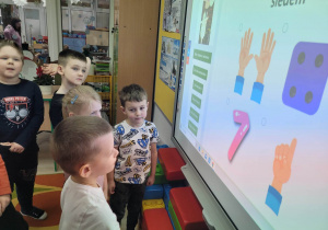 Dzieci z grupy Biedronek rozwiązują zadania matematyczne na tablicy multimedialnej.