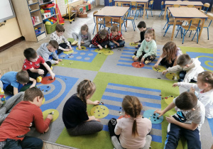 Dzieci z grupy "Słoneczek" siedzą na dywanie w trakcie zabawy z przeliczaniem guzików.