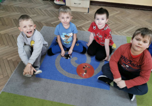Hubert, Oliwier, Krzyś i Hubert M. siedzą na dywanie i prezentują cyfrę 5 ułożoną z guzików.
