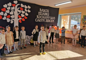 Dzieci stoją na tle dekoracji, Krzysio wyszedł na środek aby zacząć część artystyczną przygotowaną dla babć i dziadków.