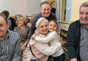 Uśmiechnięty Karolek pozuje do zdjęcia przytulając się z babcią, dziadek Karolka stoi za nimi.