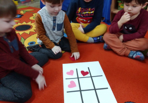 Grupa chłopców podczas gry w „kółko i krzyżyk” z różowymi i czerwonymi sercami.