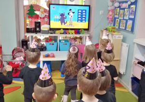 Dzieci stoją w rozsypce przed telewizorem i naśladują „koci taniec”.