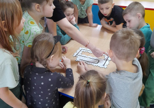 Dzieci zgromadzone wokół stołu oglądają drogę dla ozobota stworzoną przez puzzle Edu Sense, która wskazuje nauczyciel.