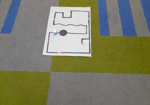 Na środku dywanu leży plansza z drogą, po której porusza się ozobot.
