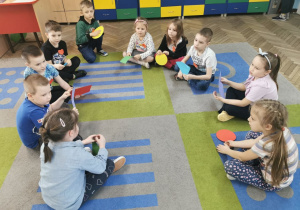 Dzieci z grupy "Słoneczka" siedzą na dywanie trzymają w rękach kolorowe figury o różnej wielkości.