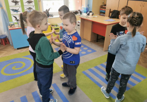 Dzieci z grypy "Słoneczka" stoją w parach na dywanie w trakcie zabawy ruchowej wykonując wskazane ćwiczenia.