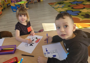 Zuzia i Antoś z grupy Biedronek siedzą przy stoliku. Dzieci tworzą pracę plastyczną opartą na figurach geometrycznych.