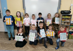 Dzieci z grupy "Słoneczek" stoją przed tablicą multimedialną i prezentują swoje zakodowane prace plastyczne.