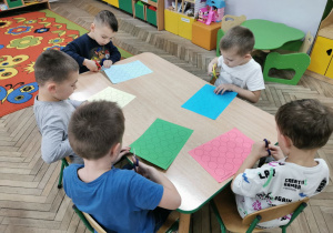 Chłopcy z grupy "Biedronek" siedzą przy stoliku i wycinają kolorowe kółeczka.