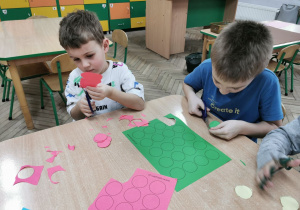 Eryk i Franek siedzą przy stoliku i wycinają różowe i zielone kółeczka.