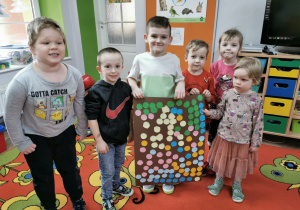 Arek, Bartek, Franek, Matvij, Zlata i Łucja stojąna dywanie i prezentują swoją wspólną pracę wykonaną z kolorowych kółek.
