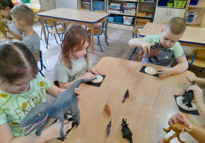 Dzieci siedzą przy stole i wykonują odcisk stopy dinozaurów w masie solnej.