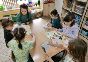 Sześcioro dzieci siedzi przy stole i ogląda książki o dinozaurach.