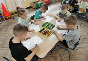 Pięcioro dzieci koloruje przy stole obrazek dinozaura według kodu.