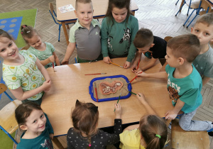 Dzieci zgromadzone są wokół stołu, na którym leży taca z odkopanym szkieletem dinozaura.